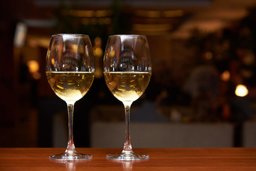 Two glasses of white wine with a reflection on the bar.