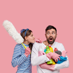 Vertical shot of dissatisfied woman looks angrily at husband, reproaches of laziness, carries...