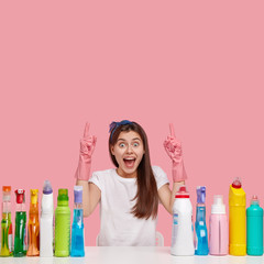 Pleased optimistic woman has happy facial expression, points above with fore fingers, advertises...