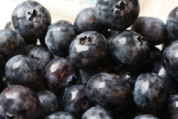 A close up photograph of a pile of shiny fresh blueberries. against a white background 