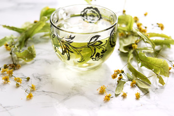 A cup of lime tea on a marble table. Dry leaves of linden leaves next to the cup.