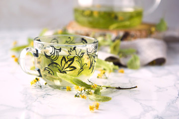 A cup of lime tea on a marble table. Dry leaves of linden leaves next to the cup.