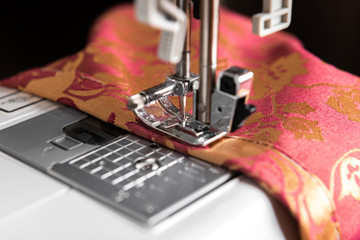The sewing machine's foot with a needle sews red fabric with flowers. 