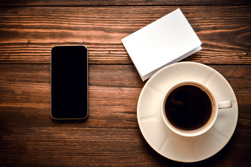 phone with a cup of coffee and white paper lies on a wooden background