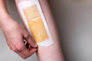 Leg waxing. Removing hair from legs on gray background.