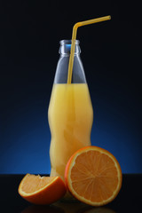 Orange juice in bottle and orange fruit on gradient blue background