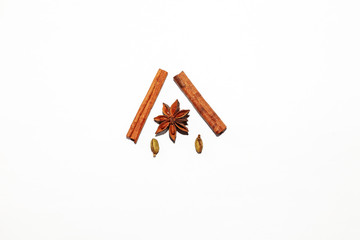Composition of spicy fragrant spices used for making mulled wine: two sticks of brown cinnamon and anise star between them close-up with seeds of cardamon. Organic element of decor.
