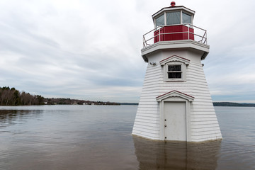 Fototapeta na wymiar A lighthouse surrounded by water. Flood waters have risen part way up the door. Overcast sky.