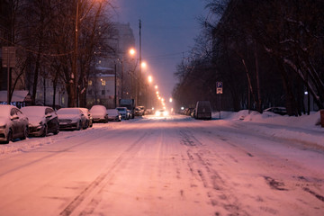 city road covered with snow with cars on the sidelines in winter season b