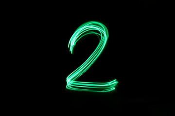 Long exposure, light painting photography.  Single number two in a vibrant neon green colour against a black background - obrazy, fototapety, plakaty