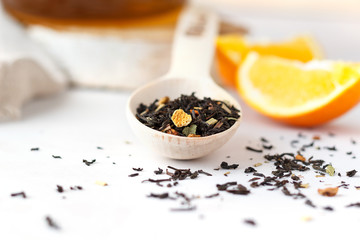 Fototapeta na wymiar A wooden spoon with dry leaves of black tea with orange peel on the table.