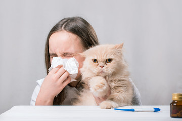 A girl holds a cat and blowing his nose in a paper handkerchief