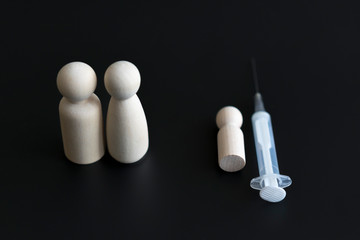 child vaccination concept. Failure of vaccines leads to death. wooden figures of parents of children and a syringe on a black background.
