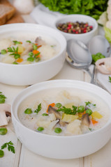 Cheese cream soup with cauliflower, mushrooms and green peas in a bowl on a white wooden background.
