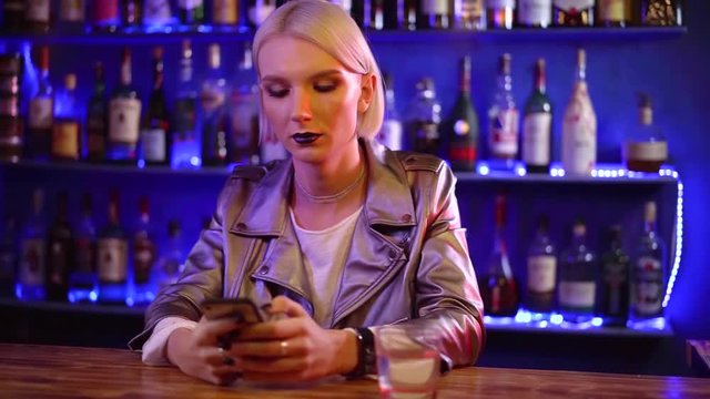 young transsexual man is dressed like a woman is typing sms by mobile phone sitting in a bar