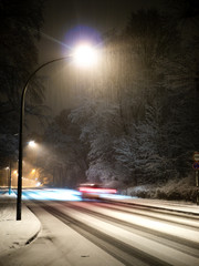 Car with motion blur driving on a snowy street with street lights at night