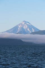 View of Vilyuchinsky volcano (also called Vilyuchik) from tourist boat. The cloud lies on the coastal cliffs. Vilyuchinsky is a stratovolcano in the southern part of Kamchatka Peninsula, Russia.