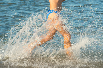 A sexy young brunette woman or girl wearing a bikini running through the surf on a deserted tropical beach with a blue sky. Young woman running by the sea.