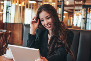 Beautiful charming brunette happy asian girl with tablet at table in cafe, student, freelancer or young manager