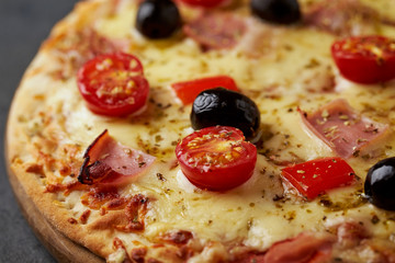 Pizza with ham, mozzarella cheese, cherry tomatoes, red pepper, black olives and oregano. Home made food. Concept for a tasty and hearty meal. Black stone background. Close up.