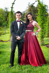 Beautiful woman in red gown leaning on handsome man in tuxedo in pretty park setting for prom photographs
