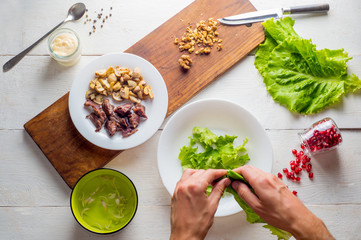 male hands tearing lettuce leaves over a plate. ingredients for cooking meat dishes on wooden white background