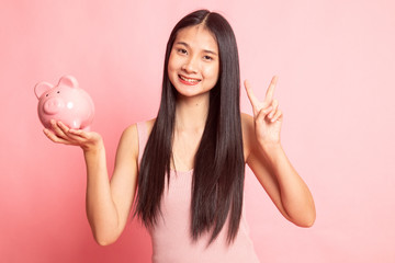 Asian woman show victory sign with pig coin bank.