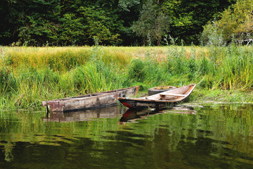 Two old boats on the shore are tied to an old car wheel, on a background of green grass a sunny summer day