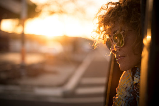 Beautiful sunny sunset time portrait for cute lady smiling and enjoying the feeling with the freedom outdoor - curly hair in the wind and sunglasses for travel concept image