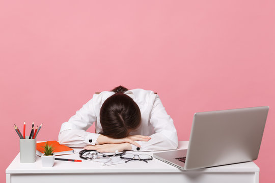 Female doctor laid her head down on desk, work on computer, medical document in hospital isolated on pastel pink wall background. Woman in medical gown glasses stethoscope. Healthcare medicine concept