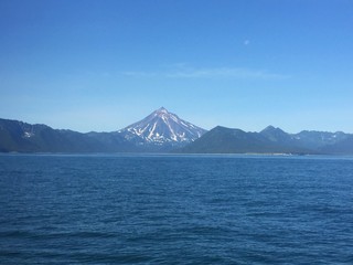 View of Vilyuchinsky volcano (also called Vilyuchik) from water. It's a stratovolcano in the southern part of Kamchatka Peninsula, Russia. Moon is visible in the sky.