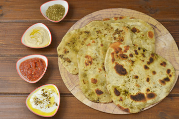 Traditional Indian Naan bread on  wooden background with small plates of some salads : labneh , hummus and matbucha (Morrocan tomato salad) , flay lay top view with copy space 