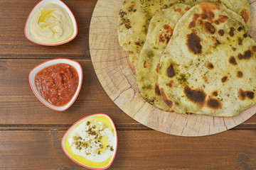 Traditional Indian Naan bread on  wooden background with small plates of some salads : labneh , hummus and matbucha (Morrocan tomato salad) , flay lay top view with copy space 