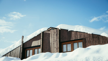 Naklejka premium Modern wood house with windows and snow on the roof, blue sky with text space