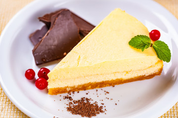 Cheesecake decorated with chocolate pieces, cranberry and mint leaves on white plate