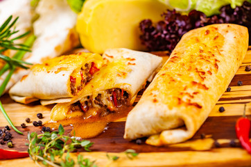 Burritos filled with meat and vegetables on wooden cutting board