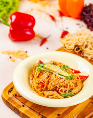 Noodles with vegetables and chicken in beige plate on wooden board