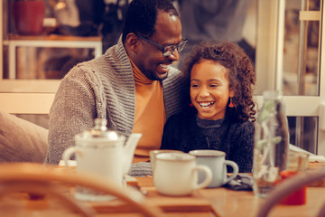 Cheerful cute curly daughter laughing while speaking with father