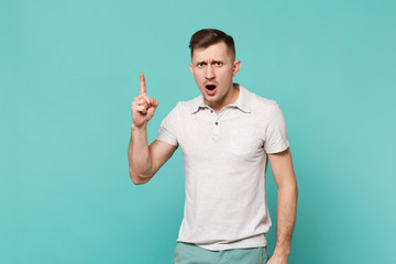 Portrait of strict young man in casual clothes pointing index finger up, swearing isolated on blue turquoise wall background in studio. People sincere emotions, lifestyle concept. Mock up copy space.