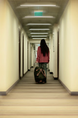 Fototapeta na wymiar Unrecognizable girl back to us is on the corridor of the hotel holding a travel bag in her hand