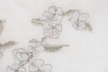 Fragment of a colorful cross-stitch embroidery, flower summer ornament on cotton canvas