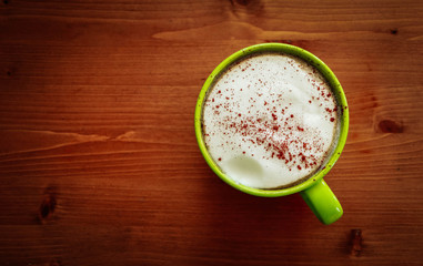 A big green cup of cappuccino coffee on the office wooden table.