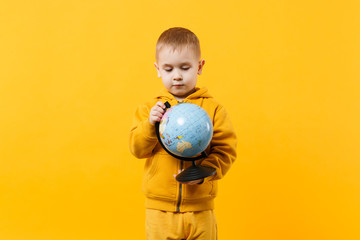 Little cute kid boy wearing yellow clothes hold Earth world globe isolated on orange wall background, children studio portrait. People sincere emotions, childhood lifestyle concept. Mock up copy space