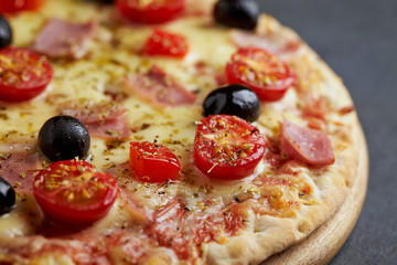 Pizza with ham, mozzarella cheese, cherry tomatoes, red pepper, black olives and oregano. Home made food. Concept for a tasty and hearty meal. Black stone background. Close up.