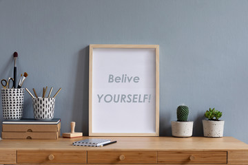 Obraz premium Scandinavian art interior with mock up photo frame on the brown wooden table with accessories, paper boxes,cacti in design pots, pencils brushes and pencils. Grey walls. Minimal concept of mockup.