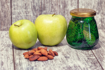 Two large green apples, a handful of almonds and a jar of jam from fir cones