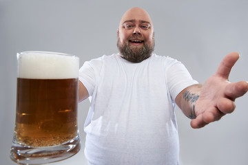 Close up of big glass of beer in hand of fat funny man