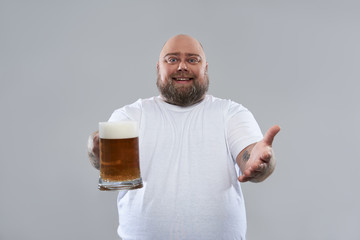 Waist up of fat bearded man looking friendly and offering beer