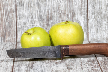 Two large green apples and a knife with a blade of Damascus steel