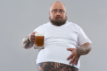 Waist up of fat man holding glass of beer and looking calm